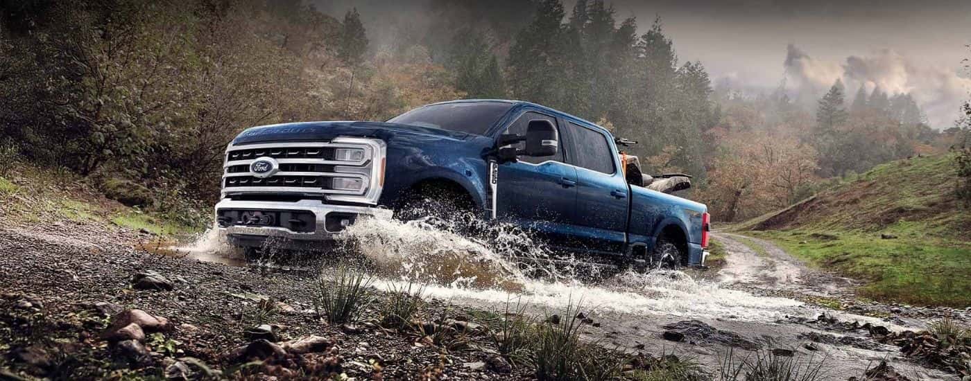 A blue 2025 Ford F-250 Tremor driving through a creek.