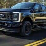 A black 2025 Ford F‑250 driving on a highway.