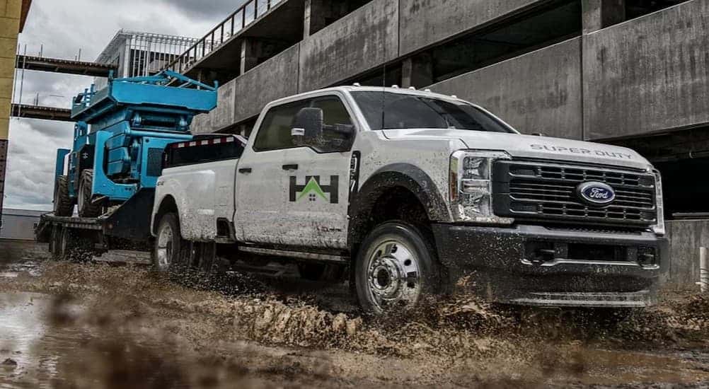A white 2025 Ford F-350 towing a scissor lift on a trailer.