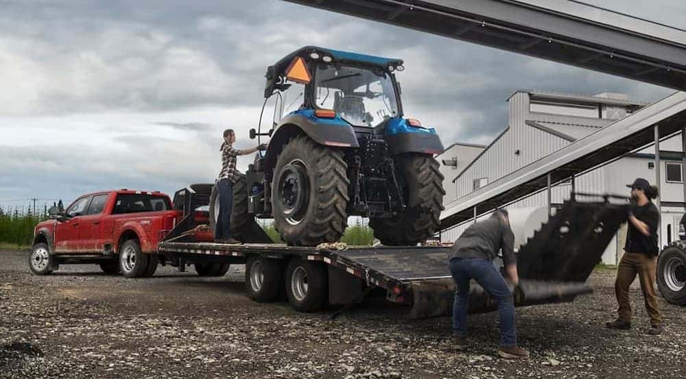 A red 2025 Ford F-450 Super Duty towing a tractor on a trailer.