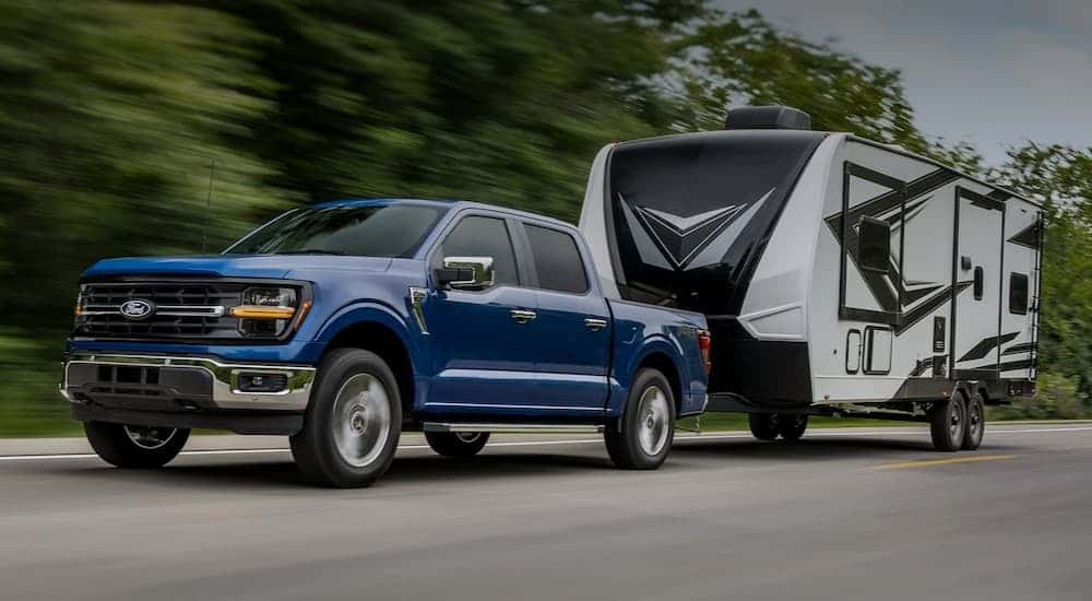 A blue 2025 Ford F-150 towing a trailer on a highway.