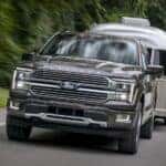 A gray 2025 Ford F-150 Hybrid Platinum towing a trailer.
