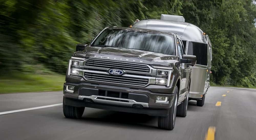 A gray 2025 Ford F-150 Hybrid Platinum towing a trailer.