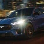 A blue used 2024 Ford Mustang Mach-E driving in a city at night