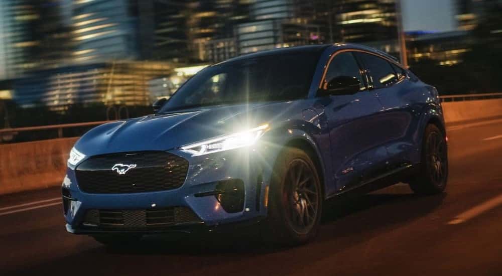 A blue used 2024 Ford Mustang Mach-E driving in a city at night