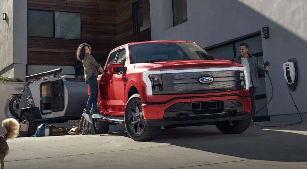 A red 2025 Ford F-150 Lightning towing a camper