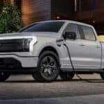 A white 2025 Ford F-150 Lightning charging outside a garage