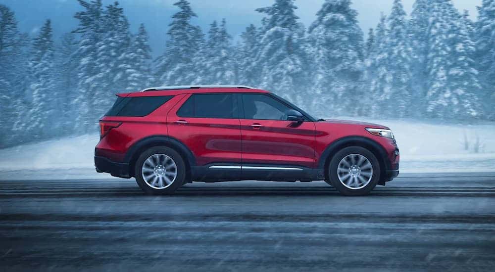 Side of a red 2023 Ford Explorer driving down a road.