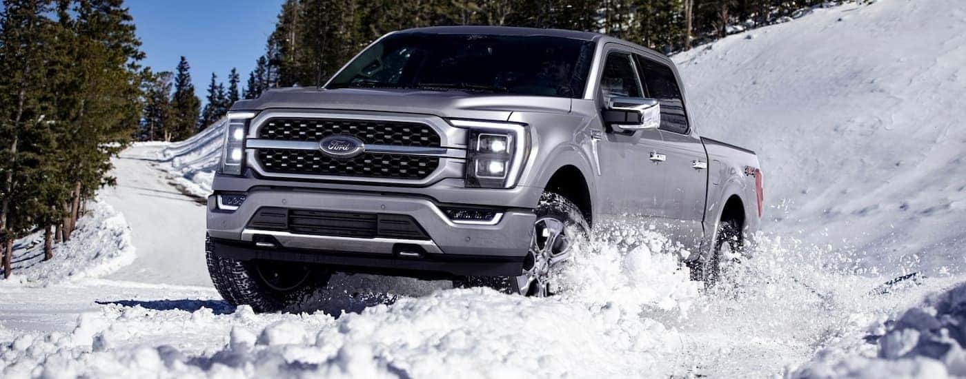 Silver 2023 Ford F-150 driving on a snowy road.