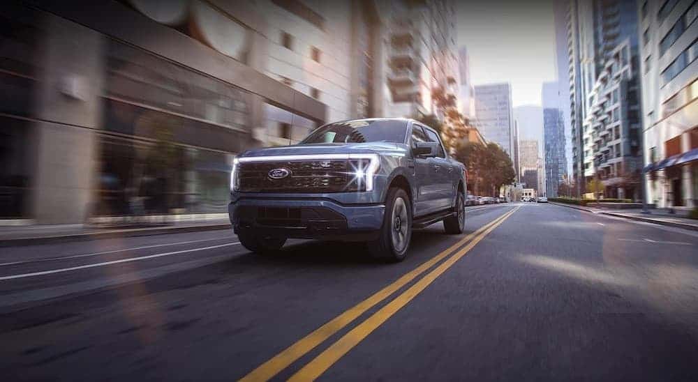 A blue 2023 Ford F-150 Lightning driving to view used trucks for sale near East Greenbush.