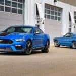 Two blue Ford Mustang Mach 1 2021 and 1969 parked in a parking lot.