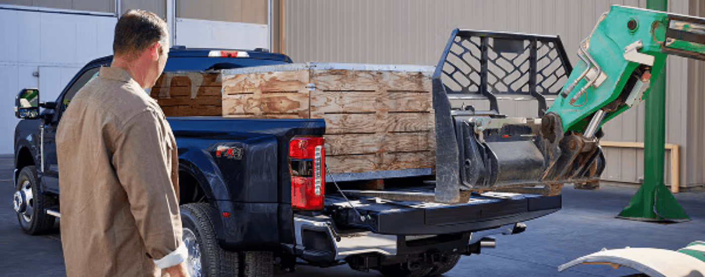 2026 Super Duty F-350 Lariat pickup in Argon Blue with the tailgate open and a fork lift loading crates into the truck bed
