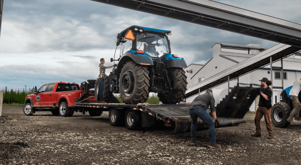 A tractor is loaded onto the trailer of a red 2026 Ford F-350 Super Duty