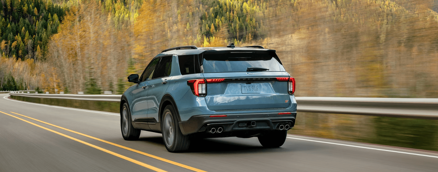 Blue 2026 Ford Explorer driving down woodland road from the back at an angle. 