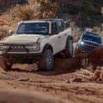 A white and blue 2026 Ford Bronco vs 2026 Jeep Wrangler off-roading