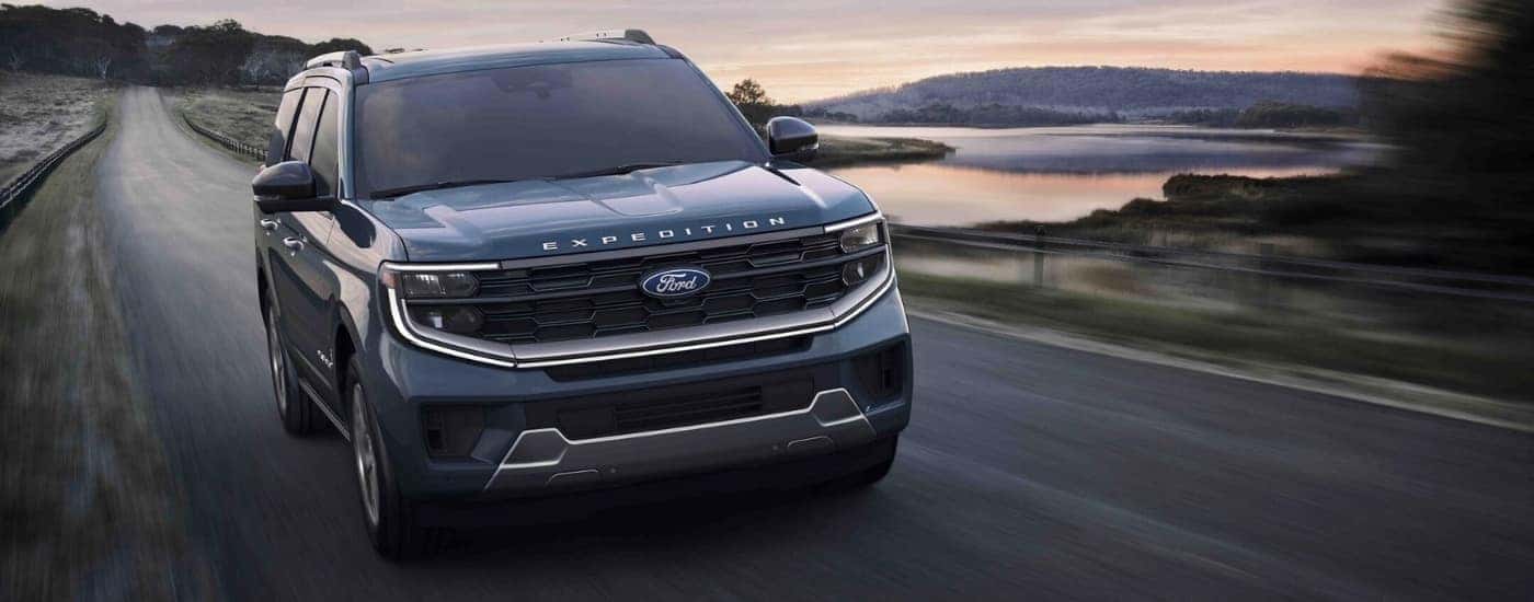 A blue 2025 Ford Expedition Platinum driving down a rural road