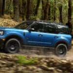 Blue 2026 Ford Bronco Sport driving off-road through a forest.