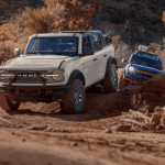 White 2026 Ford Bronco driving off-road with a blue 2026 Ford Bronco following