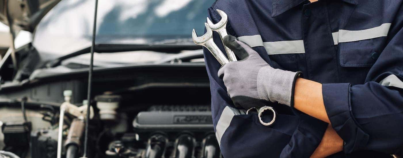 Mechanic holding wrenches in front of a vehicle