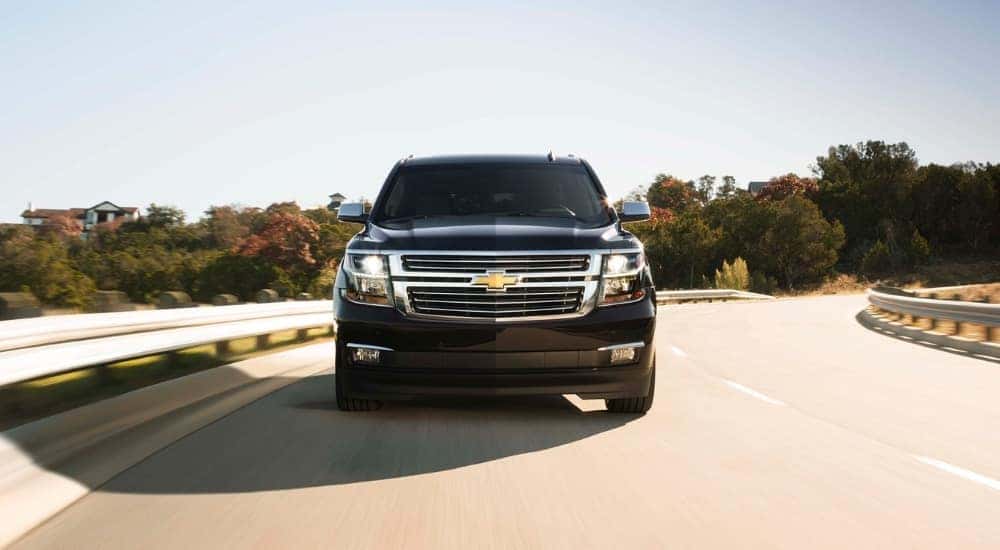A black 2017 Chevy Suburban shown driving by a guard rail.
