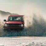 Red 2021 Ford Bronco driving through water with a big splash.