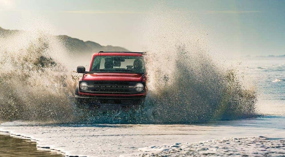 Red 2021 Ford Bronco driving through water with a big splash.