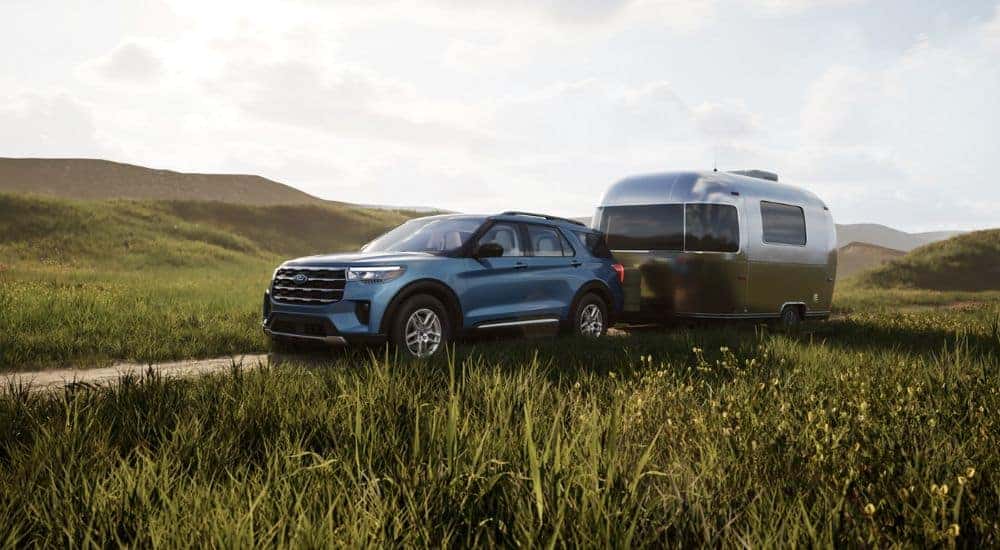 Blue 2026 Ford Explorer Active in a field towing a camper.