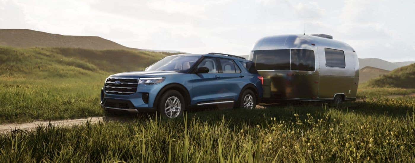 Blue 2026 Ford Explorer Active in a field towing a camper.