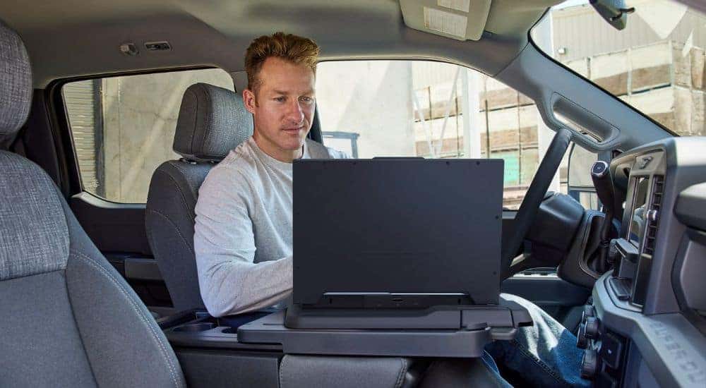 Person seated inside a parked 2026 Ford Super Duty® F-250® XL pickup using a laptop with the interior work surface feature.