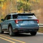 Rear view of a light blue 2026 Ford Explorer driving by trees.
