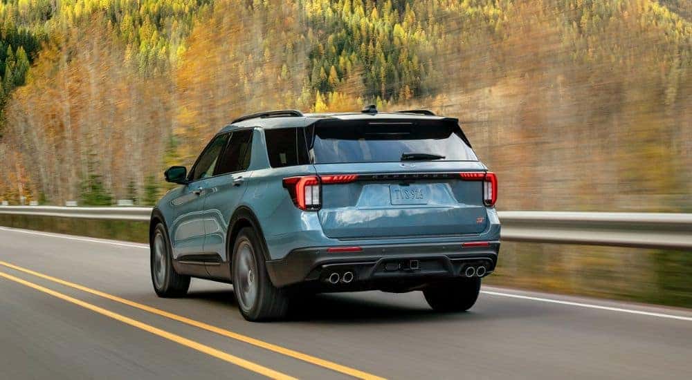 Rear view of a light blue 2026 Ford Explorer driving by trees.