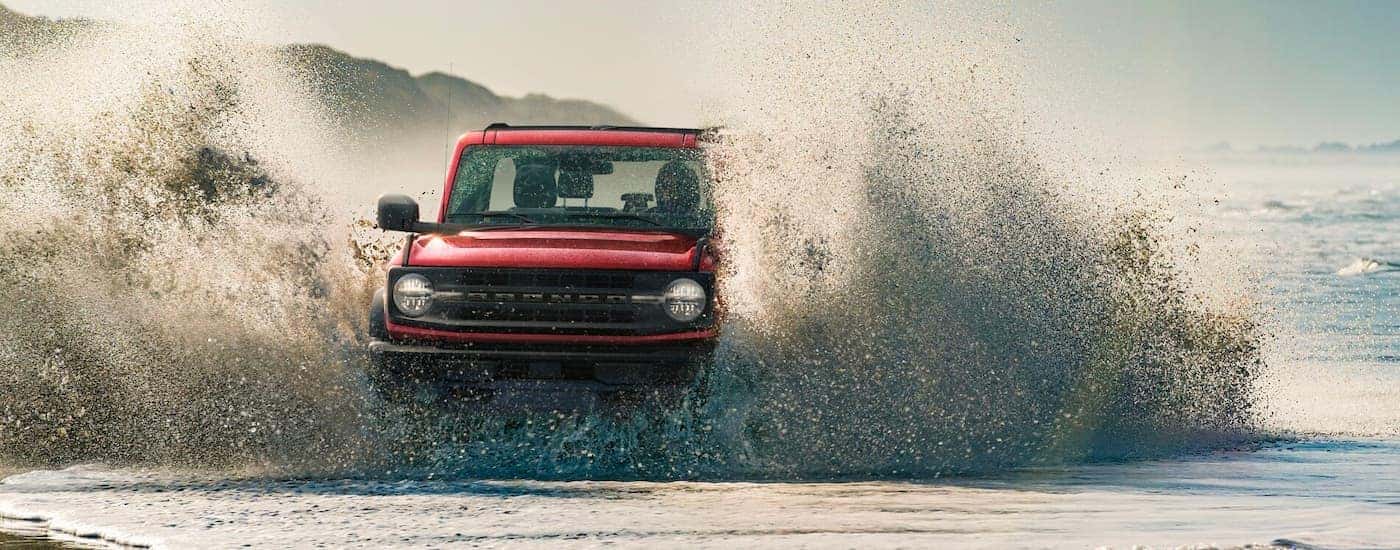 Red 2021 Ford Bronco driving through water with a big splash.