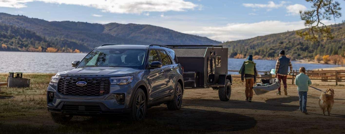 A blue 2026 Ford Explorer towing a trailer near a lake.