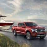 A red 2024 Ford F-150 Platinum Plus towing a boat by the ocean.