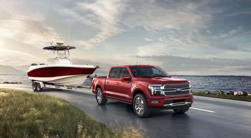 A red 2024 Ford F-150 Platinum Plus towing a boat by the ocean.
