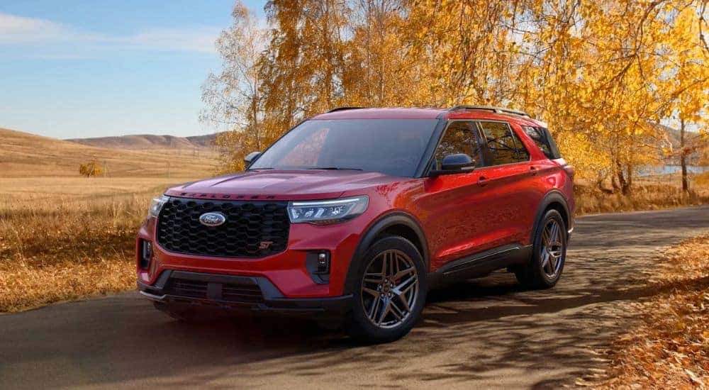 A red 2026 Ford Explorer ST shown driving a tree-lined road in autumn.