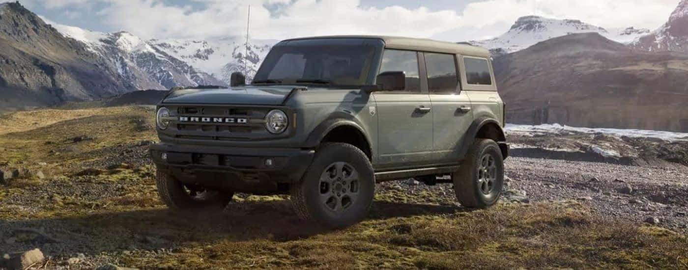 A sage green 2023 Ford Bronco Big Bend parked off-road in the mountains.