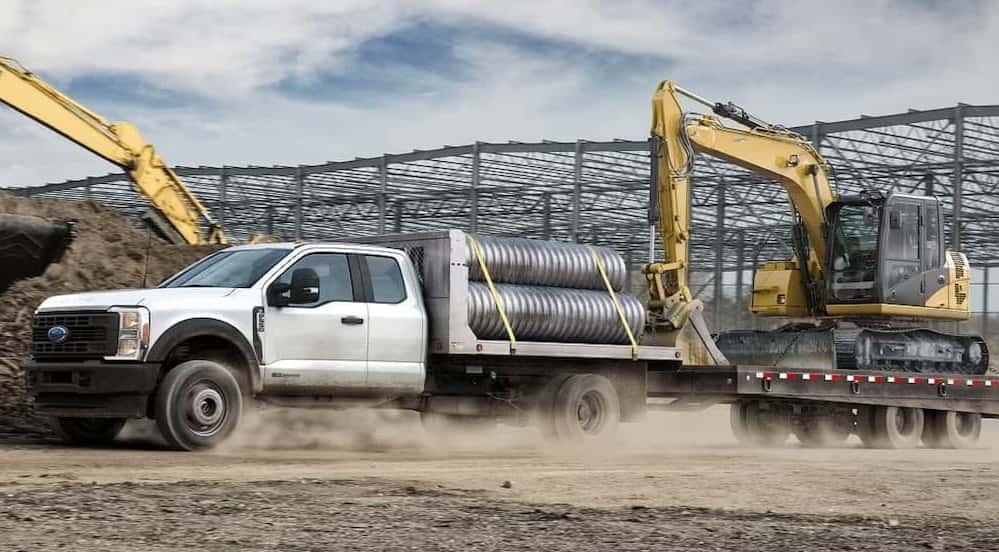 A white 2026 Ford F-350 towing heavy machinery.