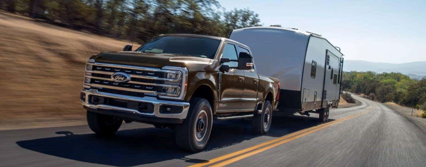 Brown 2026 Ford F-250 towing a camper down a paved road.