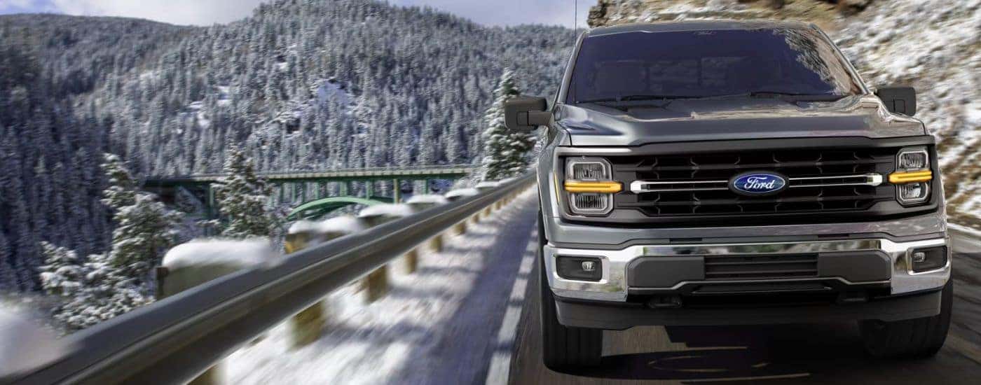 Grey 2026 Ford F-150 XLT driving on a paved road in the winter.