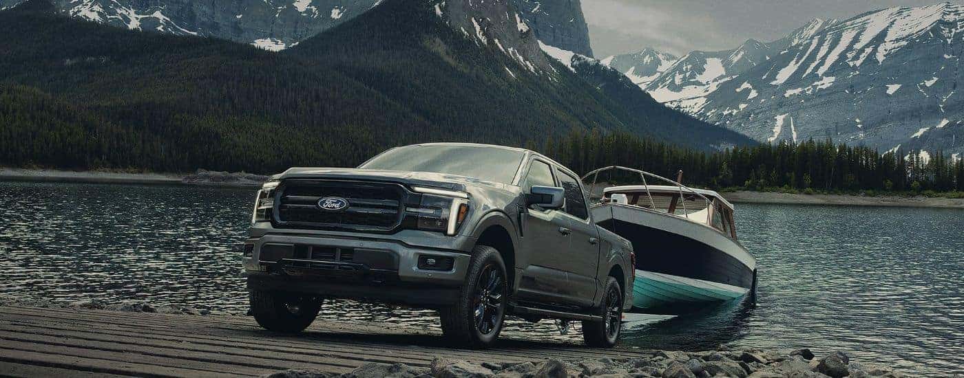Grey 2026 Ford F-150 XLT towing a boat out of a lake in the mountains.