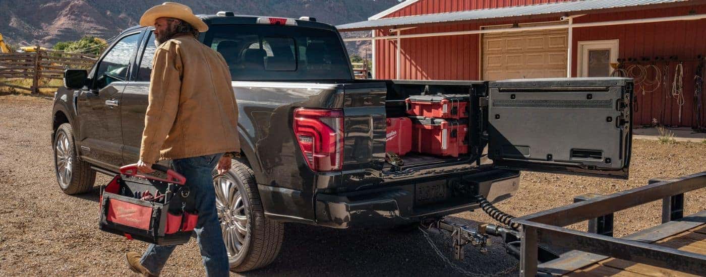 Black 2026 Ford F-150 towing a trailer with tools in the bed and a man walking away.