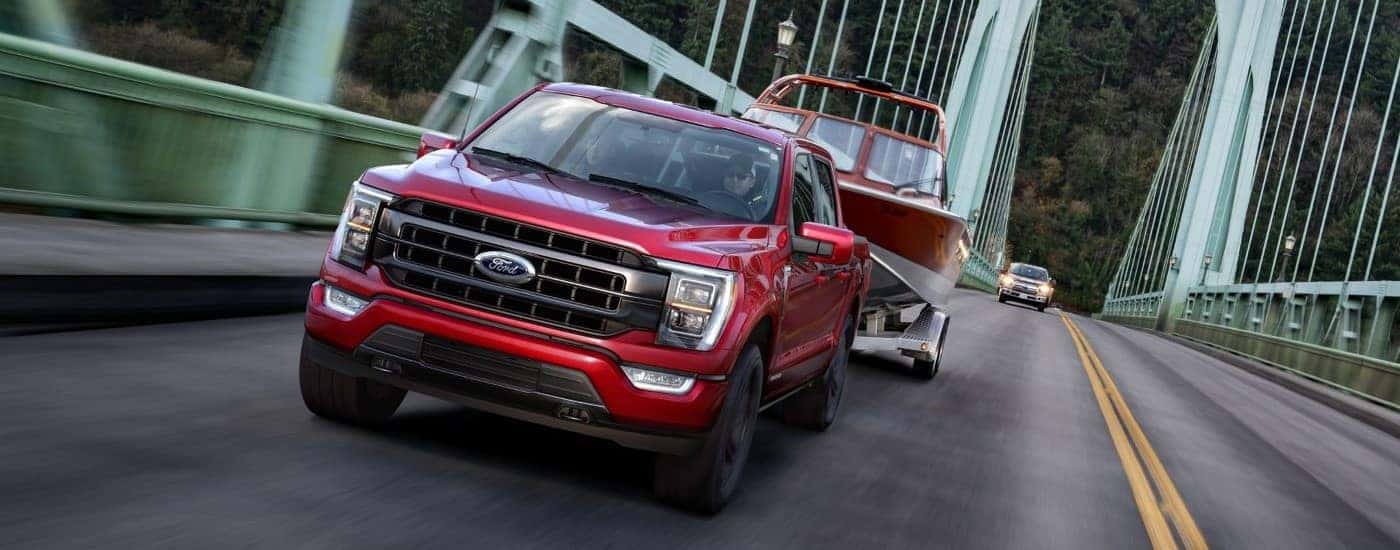 Red 2021 Ford F-150 towing a boat over a bridge.