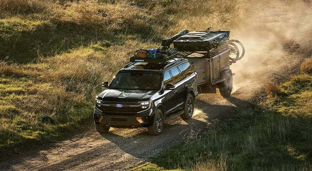 A black 2027 Ford Expedition towing a trailer on a dirt road.