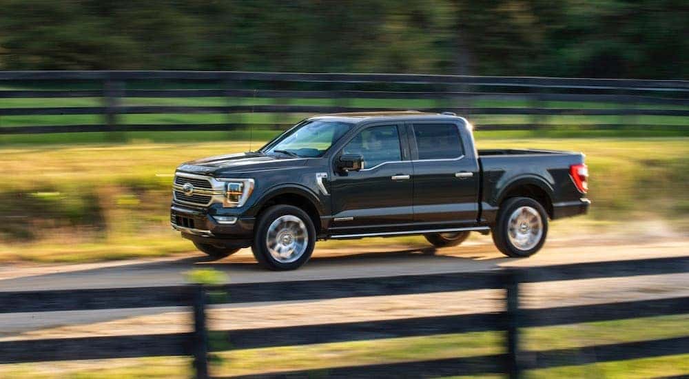 A black 2021 Ford F-150 Hybrid driving near a fence.