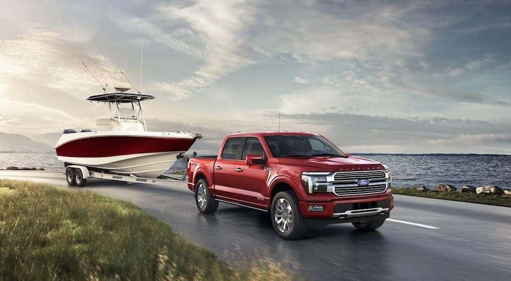A red 2024 Ford F-150 towing a boat near water.