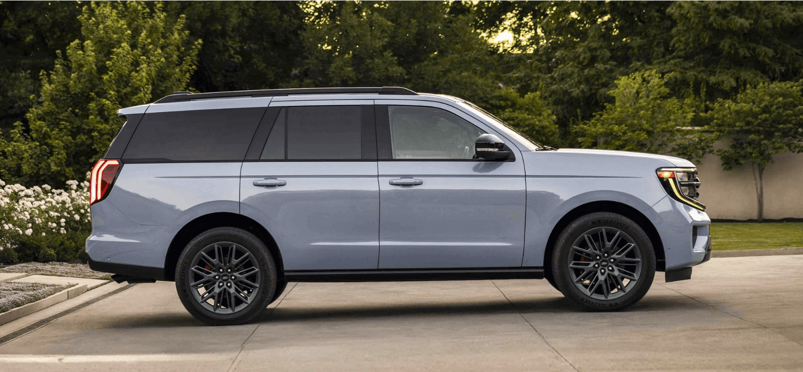 Side view of a light blue 2025 Ford Expedition SUV parked in a driveway with trees in the background.