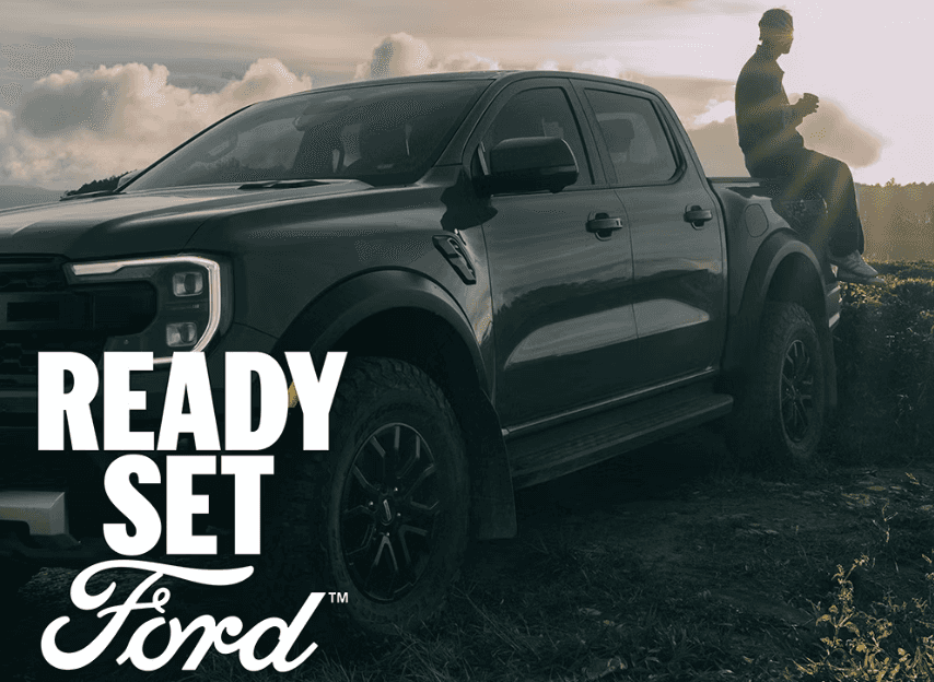 Man sitting on the tailgate of a Ford pickup truck at sunset with ‘Ready Set Ford’ text overlay.