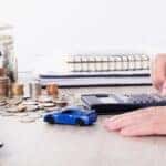 hand using calculator; cash and coins; and a toy car.
