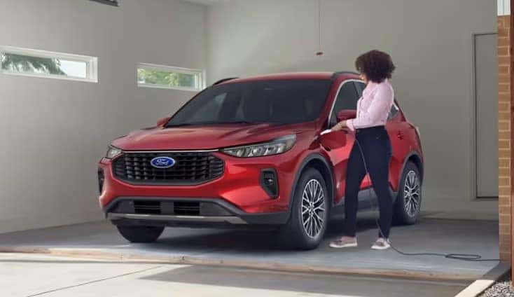 Red Ford SUV parked in a garage with a driver plugging in the charging cable.